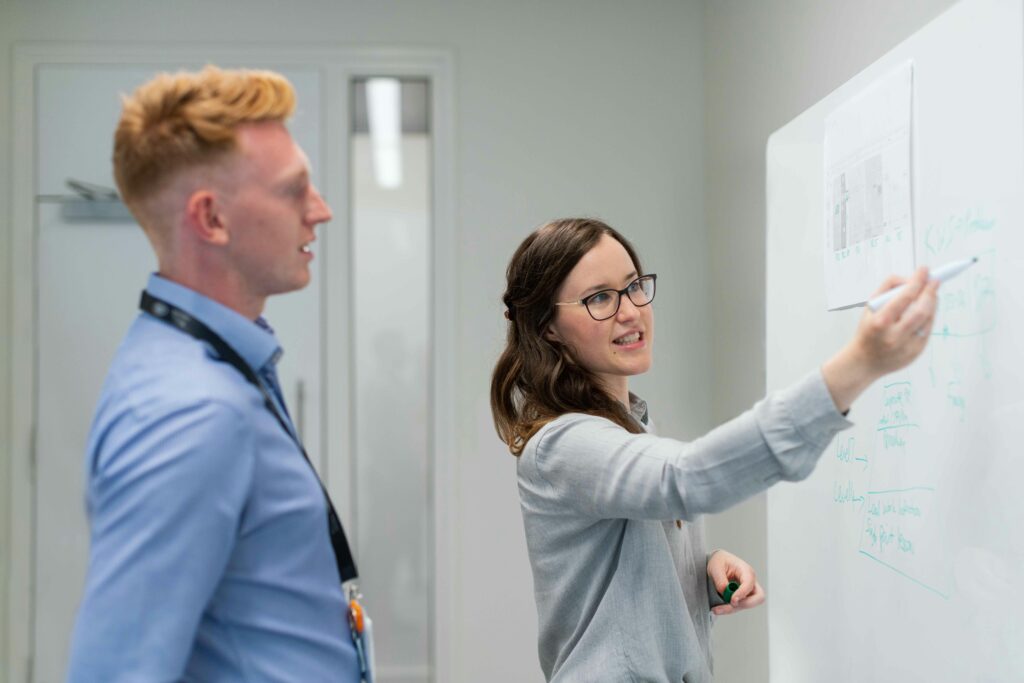 A project manager explaining project details to a coleague in front of a whiteboard