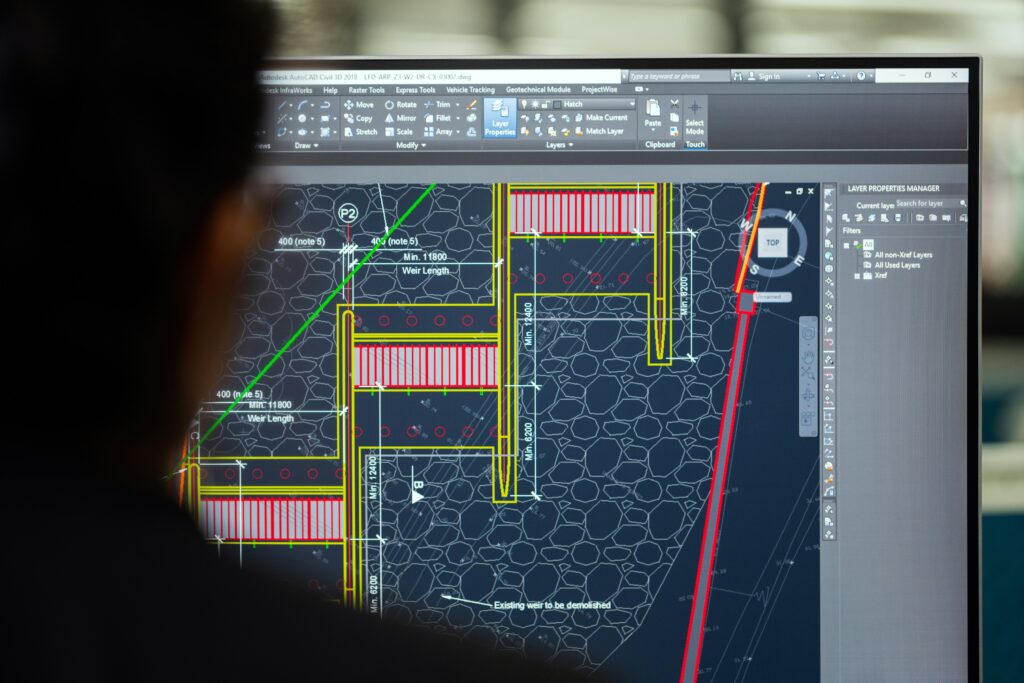 Engineer reviewing detailed CAD architectural blueprints on a computer monitor, showing technical floor plan drawings with measurements and annotations