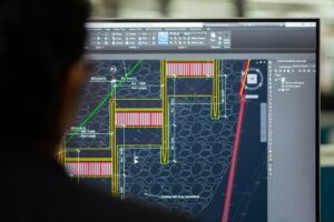 Engineer reviewing detailed CAD architectural blueprints on a computer monitor, showing technical floor plan drawings with measurements and annotations