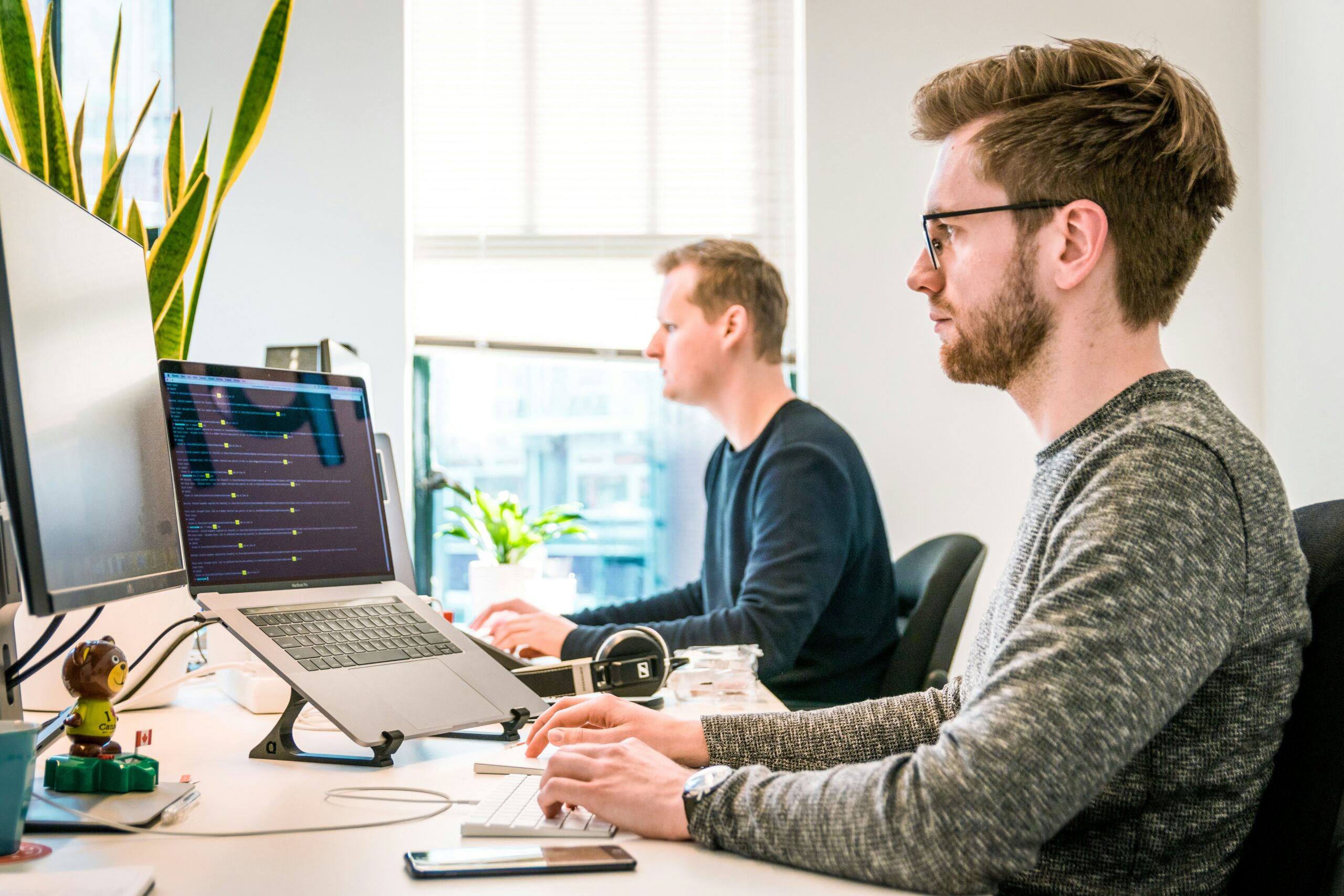 Software developers working at their desks with multiple monitors in a modern office, focused on coding and development tasks
