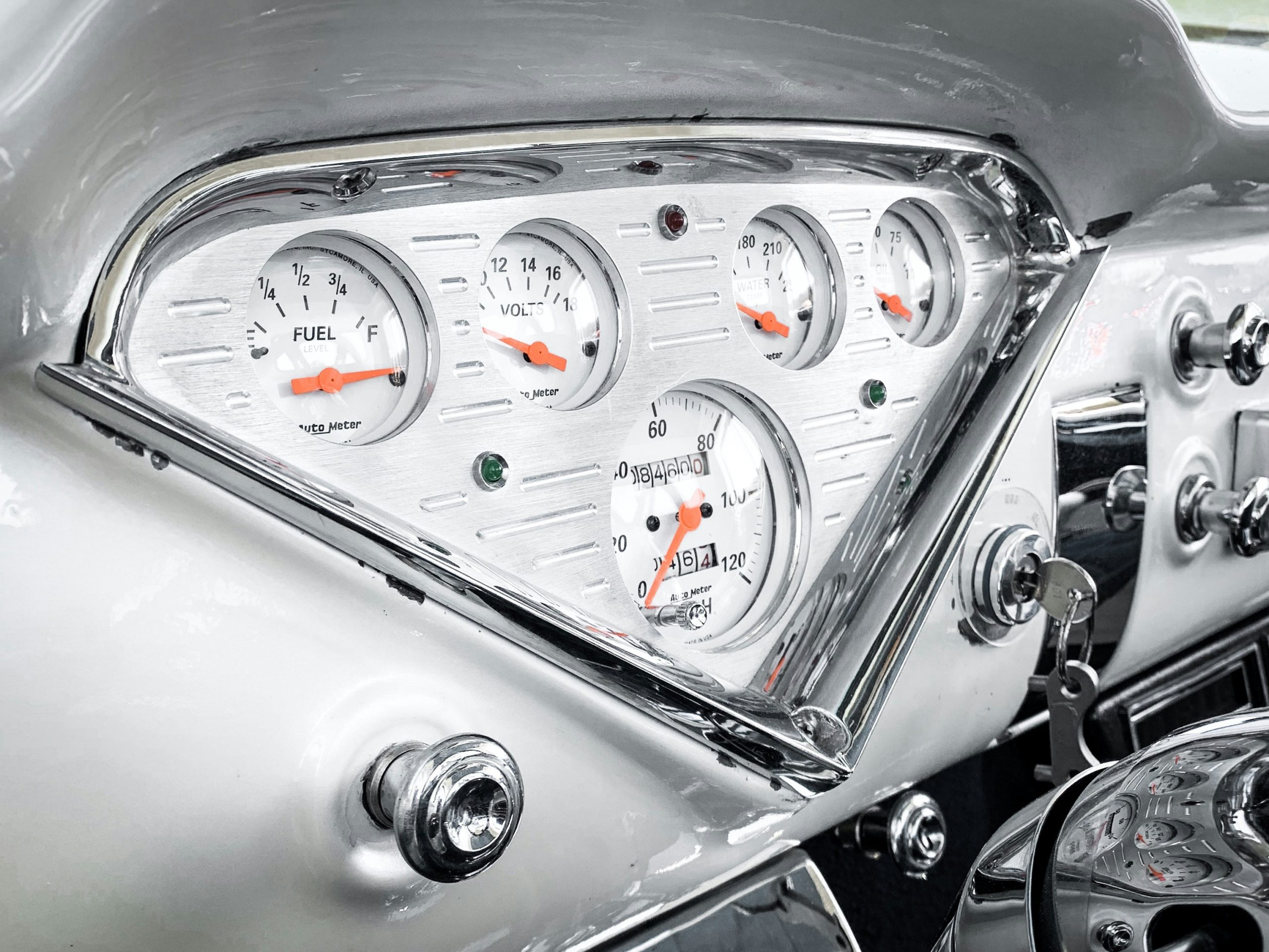 Vintage car dashboard with chrome gauges showing fuel, voltage, temperature, and speedometer