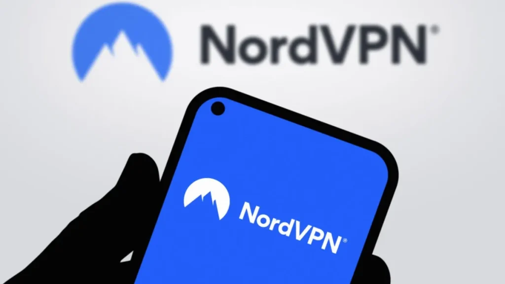 Hand holding smartphone displaying NordVPN app, NordVPN logo on a wall in the background