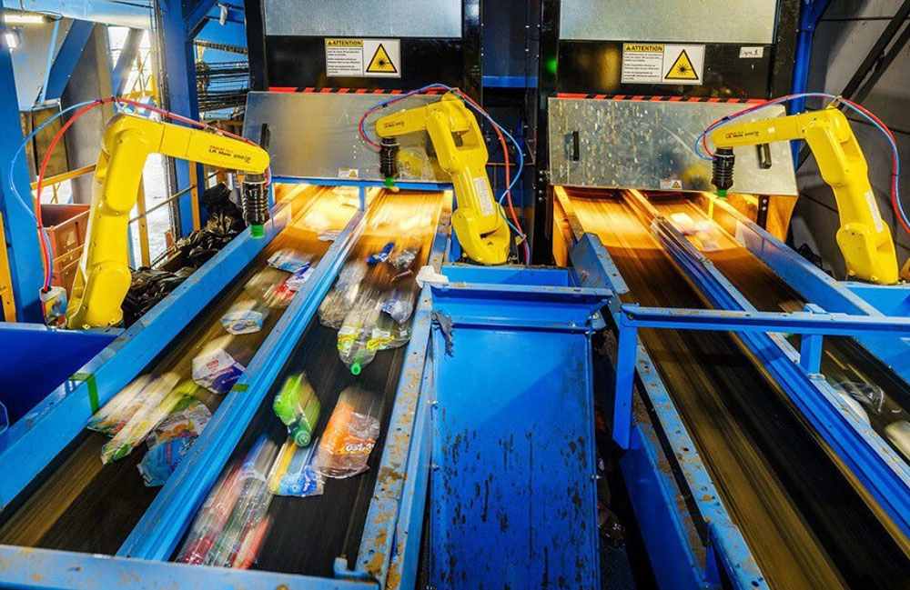 Yellow industrial robotic arms sorting waste materials on a conveyor belt system in a recycling facility