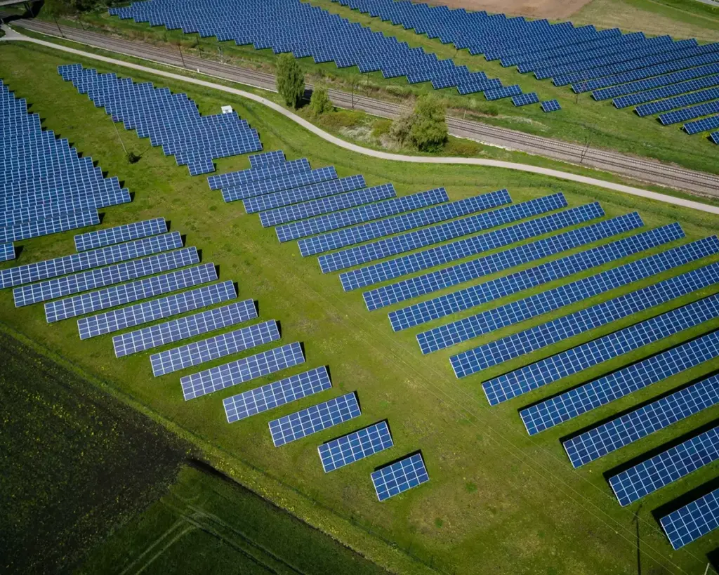 Aerial view of a large solar panel farm with rows of photovoltaic panels in a green field