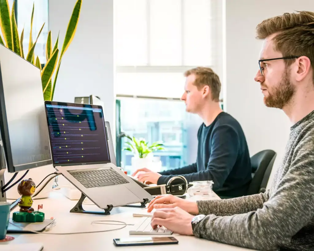 Software developers working at their desks with multiple monitors in a modern office, focused on coding and development tasks