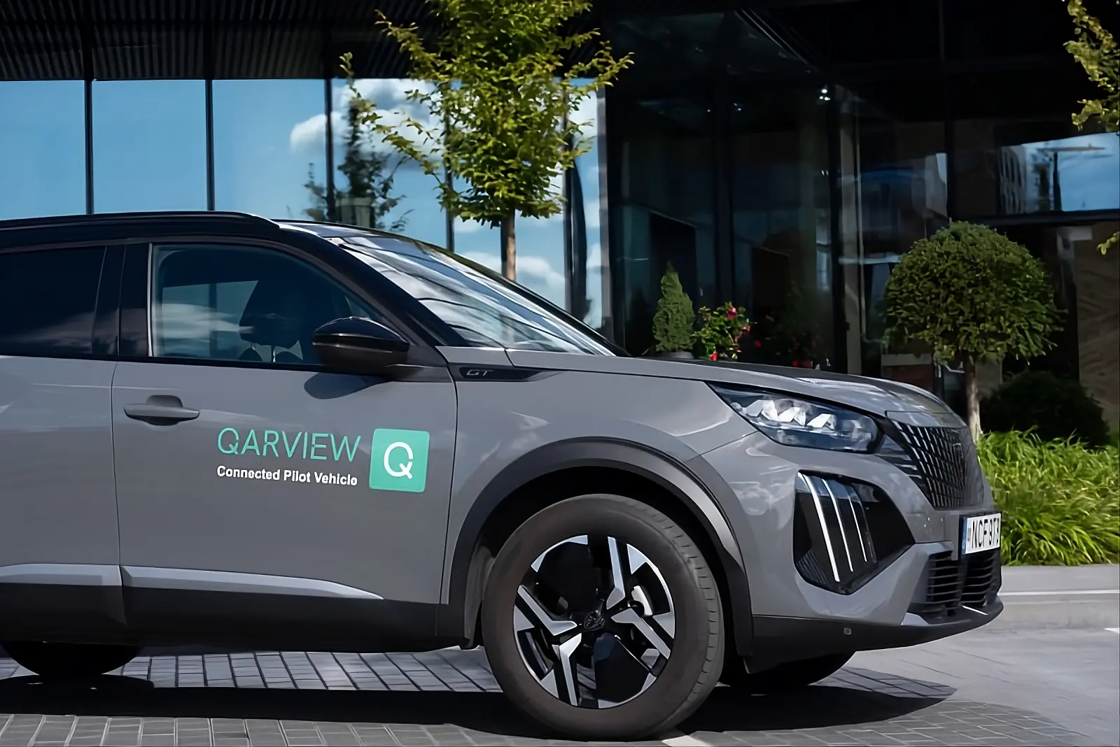 A photo of a grey Peugeot compact SUV with QarView logo, shot from the right side in an urban setting
